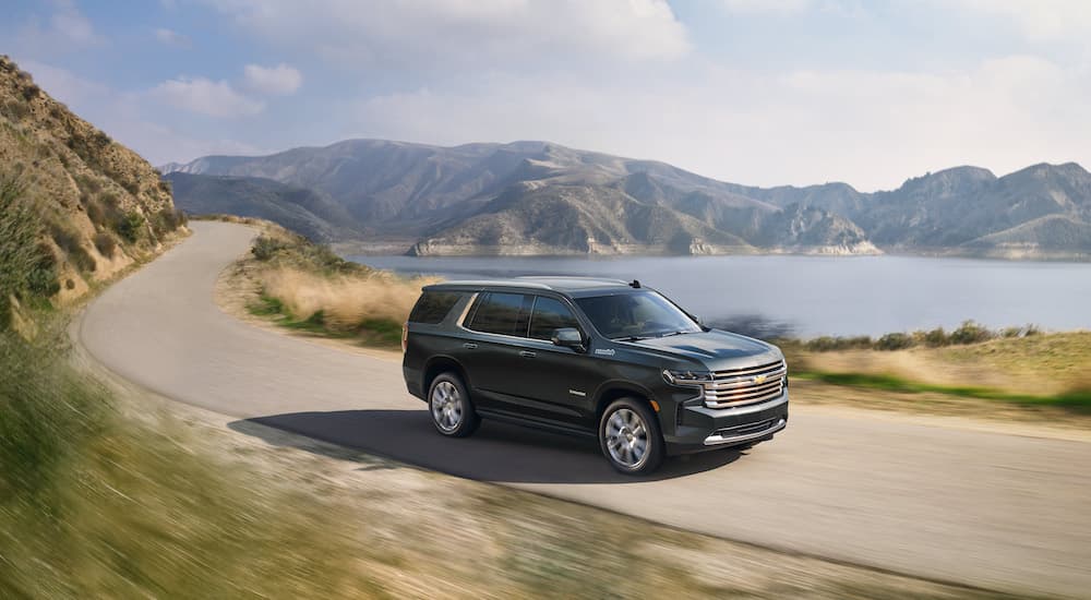 A green 2023 Chevy Tahoe High Country is shown from the side on a coastal road.