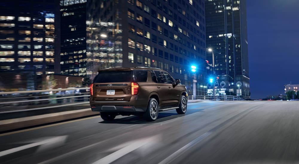 A brown 2024 Chevy Tahoe RST is shown from the rear at an angle while driving through the city after leaving a dealer that has a Chevy Tahoe for sale.