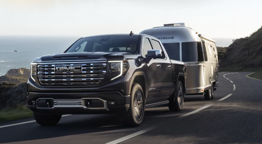 A black 2022 GMC Sierra 1500 Denali towing an Airstream trailer on the highway.