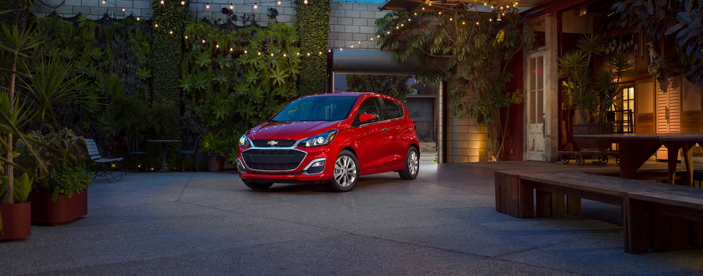 A red 2020 Chevy Spark is parked under hanging lights at dusk.