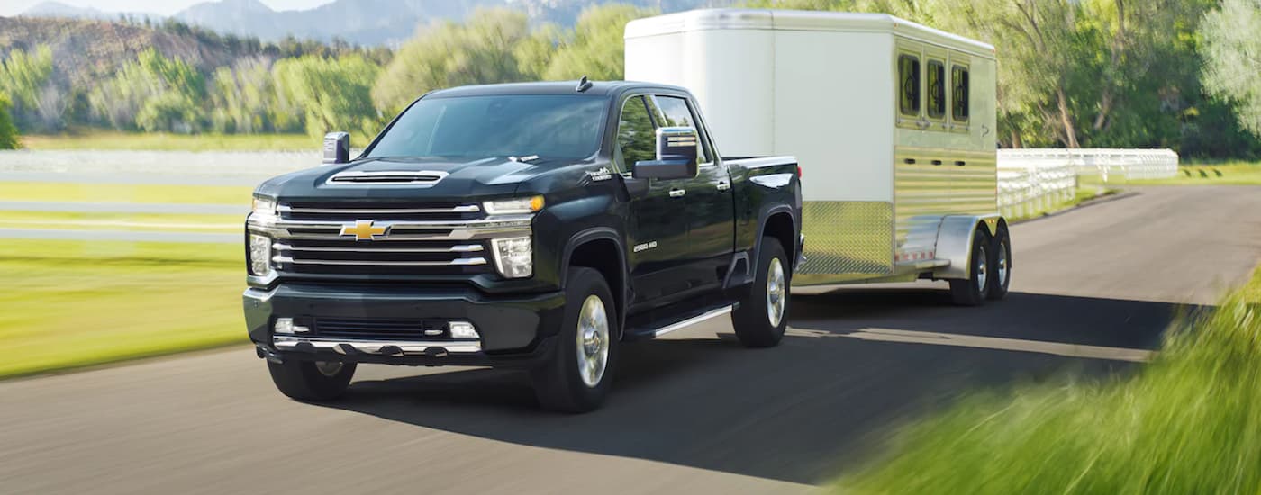 A black 2021 Chevy Silverado 2500HD is towing a trailer on a rural road.