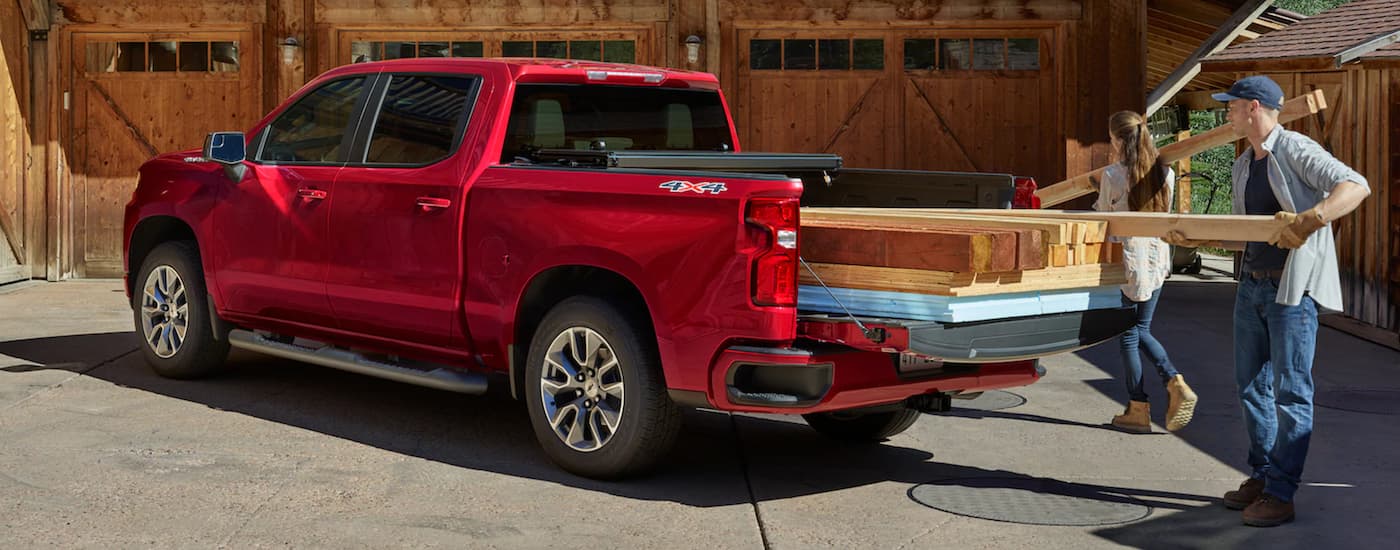 A couple is loading lumber into the bed of a red 2021 Chevy Silverado 1500.