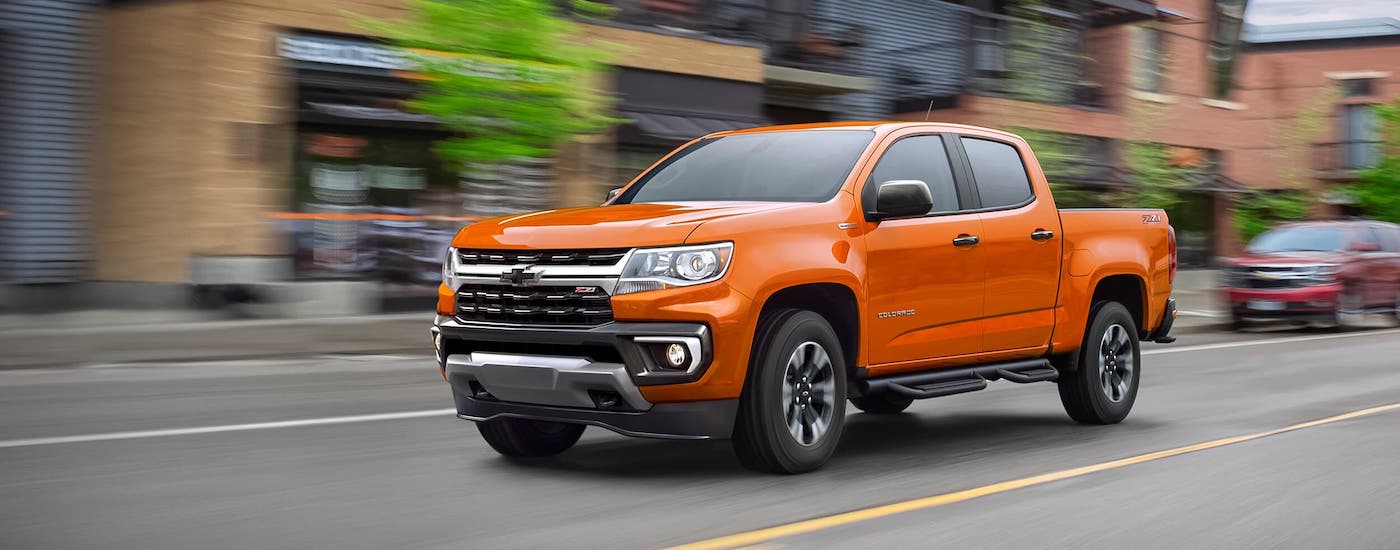 A smaller Chevy truck, an orange 2021 Chevy Colorado Z71, is driving on a city street.