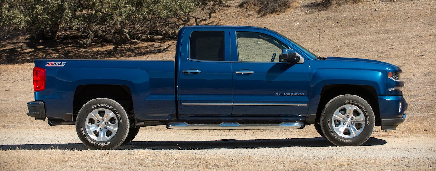 A blue 2017 Chevy Silverado 1500 is shown from the side while parked on a field of dry grass.