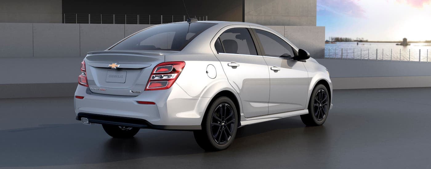 A silver 2018 Chevy Sonic from a used car dealer is parked at a modern home.