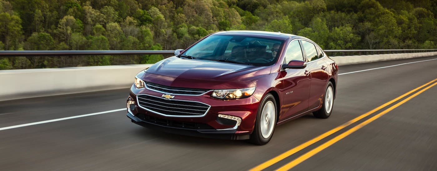 A red 2018 Chevy Malibu is driving on a highway past trees after leaving a used car dealer near me.