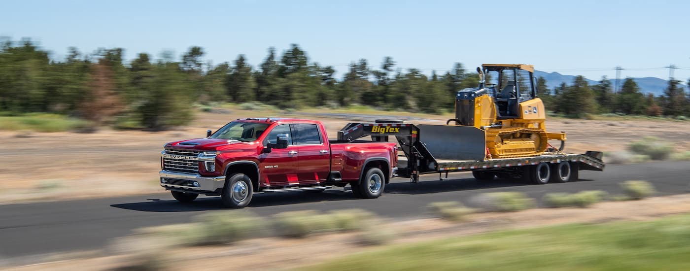 A red 2022 Chevy Silverado 3500 HD is shown from the side while towing a bulldozer.