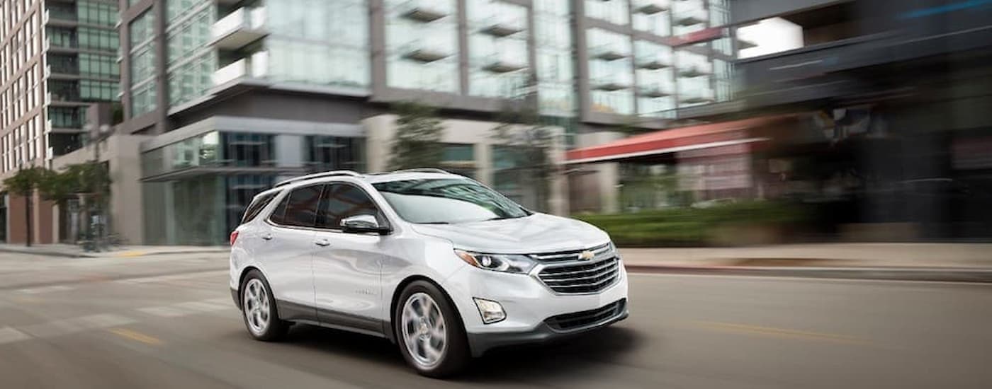 A white 2019 Chevy Equinox is shown driving on a city street after leaving a Aldine used Chevy dealer.
