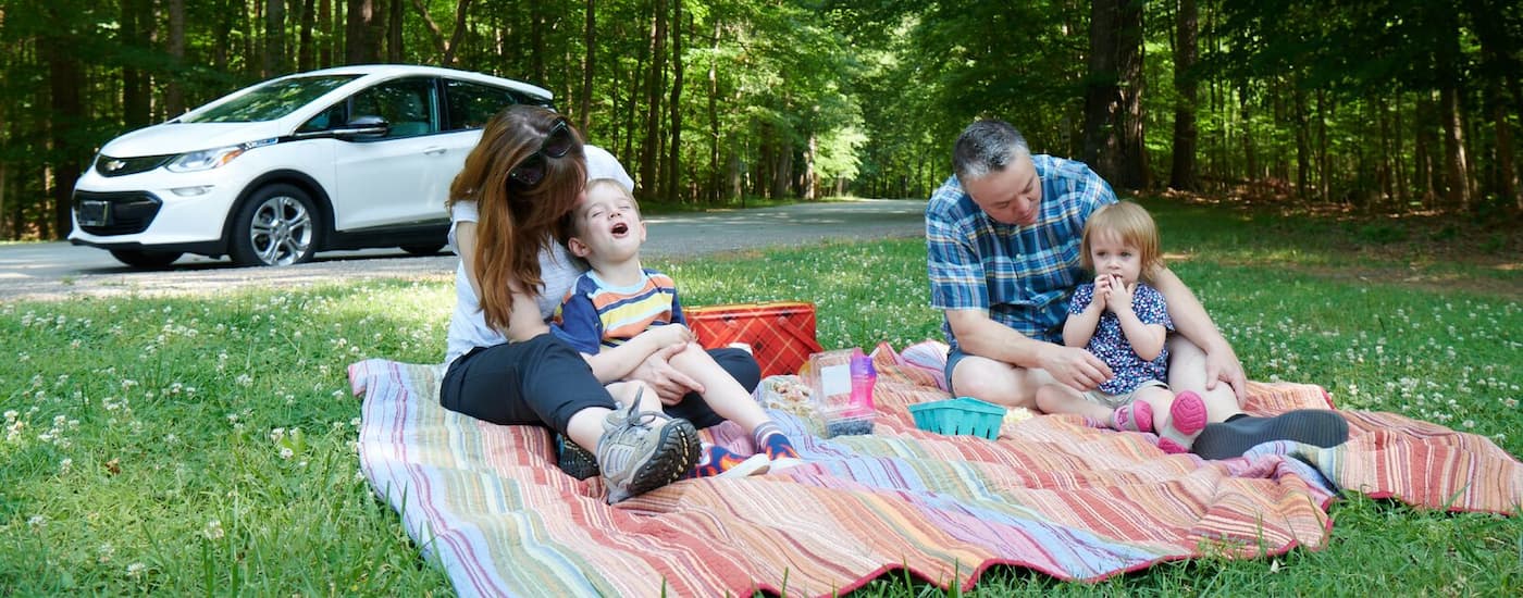 A family is shown having a picnic near a white certified pre-owned 2020 Chevy Bolt EV.