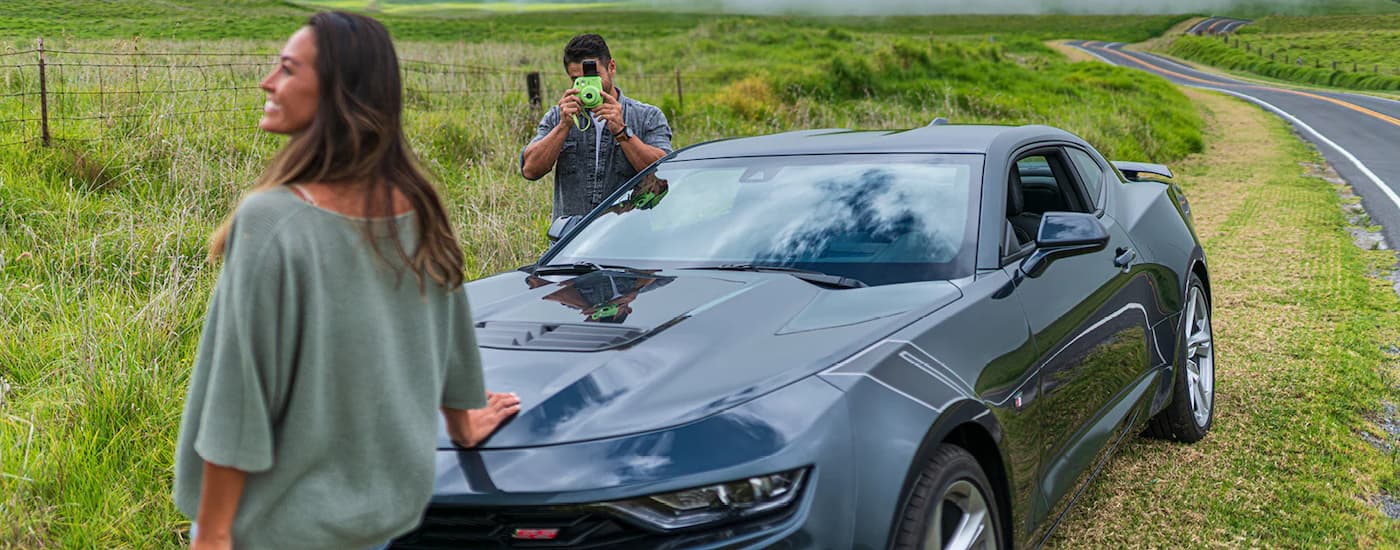 A couple is shown taking photos near a dark grey 2020 Chevy Camaro SS.