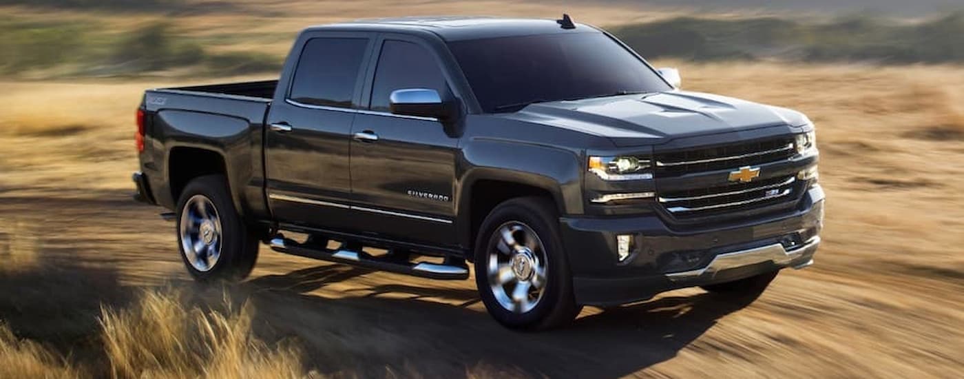 A black 2018 certified pre-owned Chevy Silverado 1500 is shown driving through a dry grassy field.