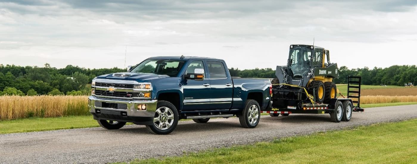 A blue 2019 Chevy Silverado 2500HD is shown towing heavy machinery after leaving a certified pre-owned Silverado dealer.