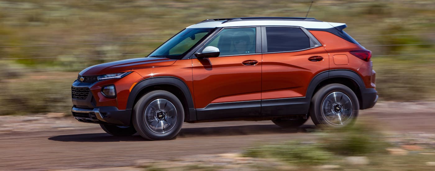 An orange 2021 Chevy Trailblazer ACTIV is shown from the side driving on a dirt road.