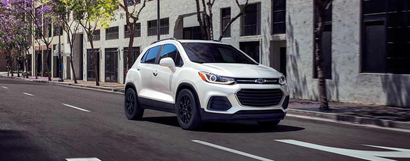 A white 2022 Chevy Trax is shown driving on a city street.