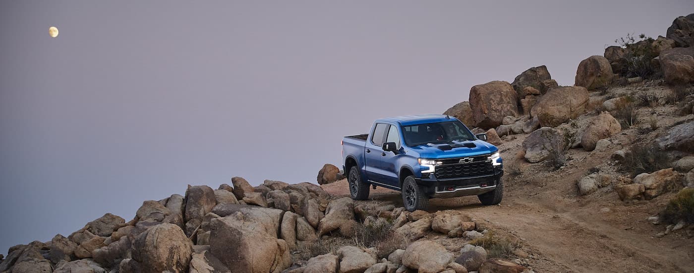 A blue 2022 Chevy Silverado 1500 ZR2 is shown on a rocky path in the mountains.