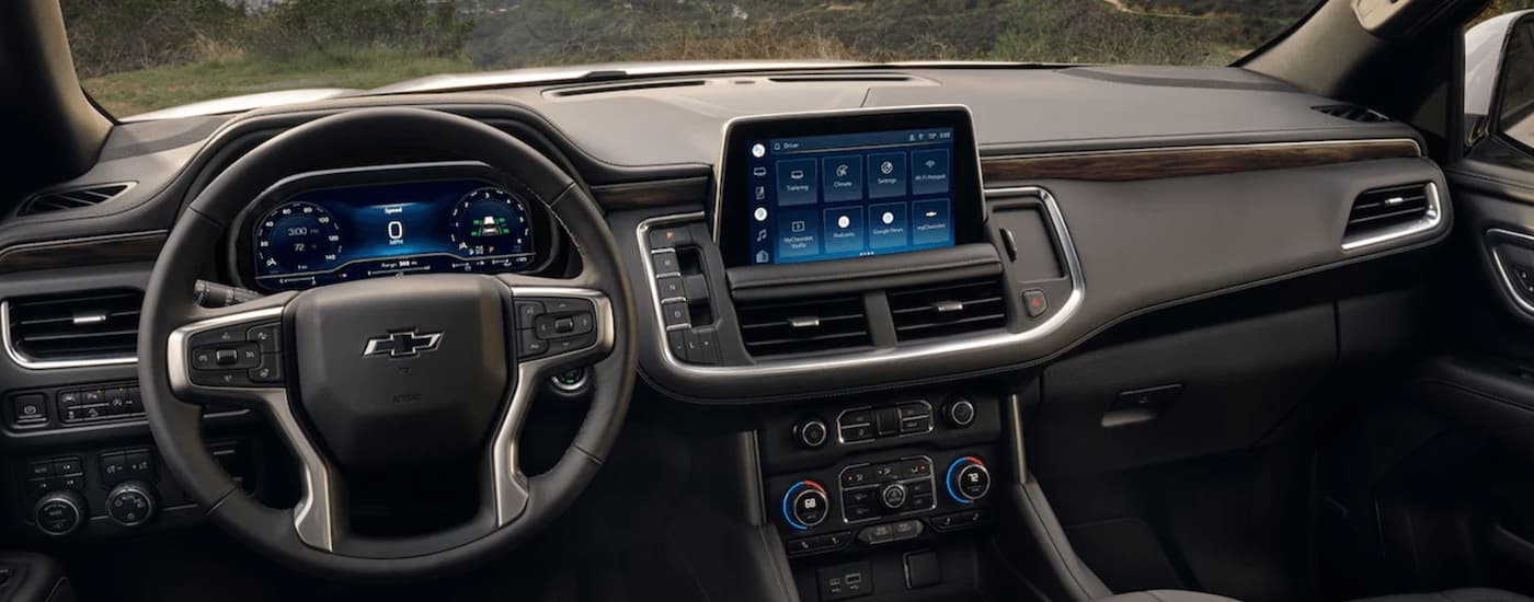 The black dashboard of a 2023 Chevy Tahoe for sale shows the steering wheel and infotainment screen.