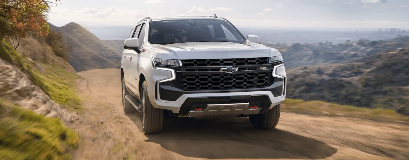A white 2023 Chevy Tahoe Z71 is shown from a front angle driving on a dirt mountain road.