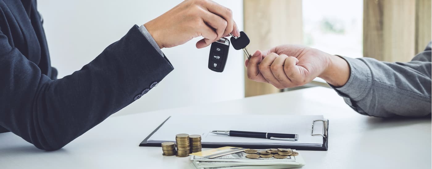A customer and car salesman are shown exchanging a car key.