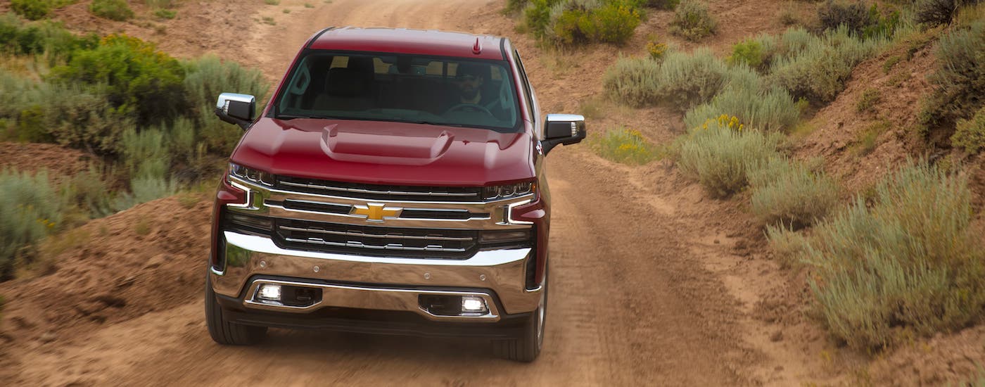 A red 2021 Chevy Silverado 1500 is shown from the front driving on a dirt road after leaving a Houston Chevy truck dealer.