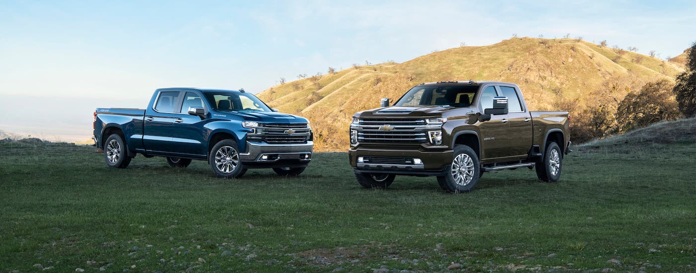 A blue 2021 Chevy Silverado 1500 and a brown 2500HD are parked on a hill.