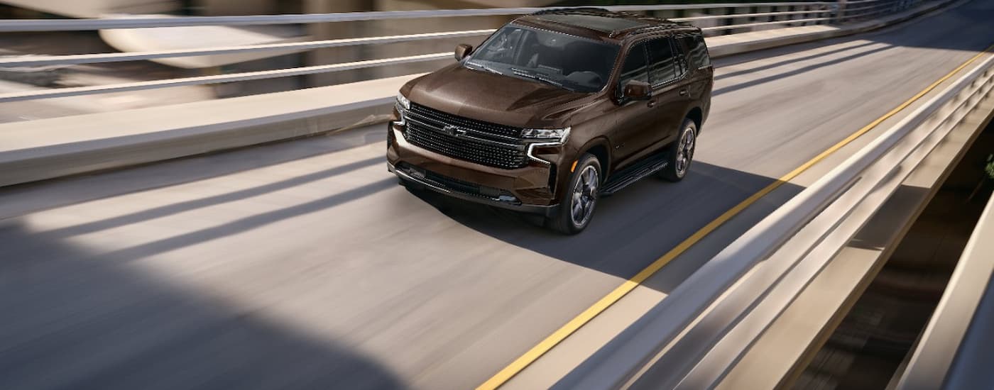 A brown 2023 Chevy Tahoe is shown driving on a highway after leaving a Magnolia Chevy dealer.