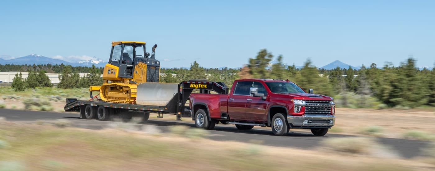 A red 2022 Chevy Silverado 3500HD is shown towing heavy machinery after visiting a pre-owned Silverado dealer.