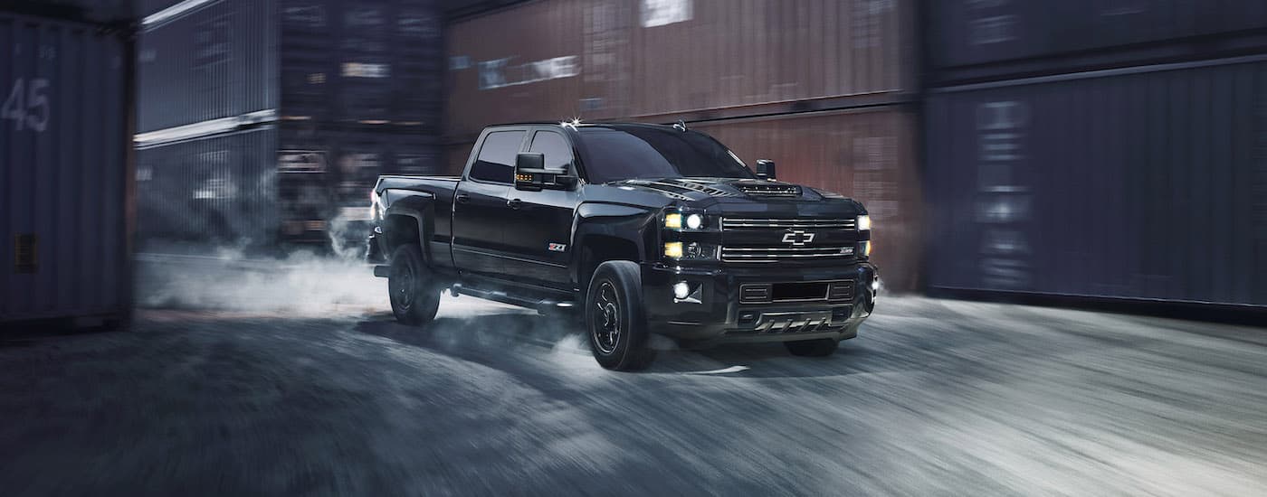 A black 2017 Chevy Silverado 2500HD Z71 is shown driving past shipping containers.