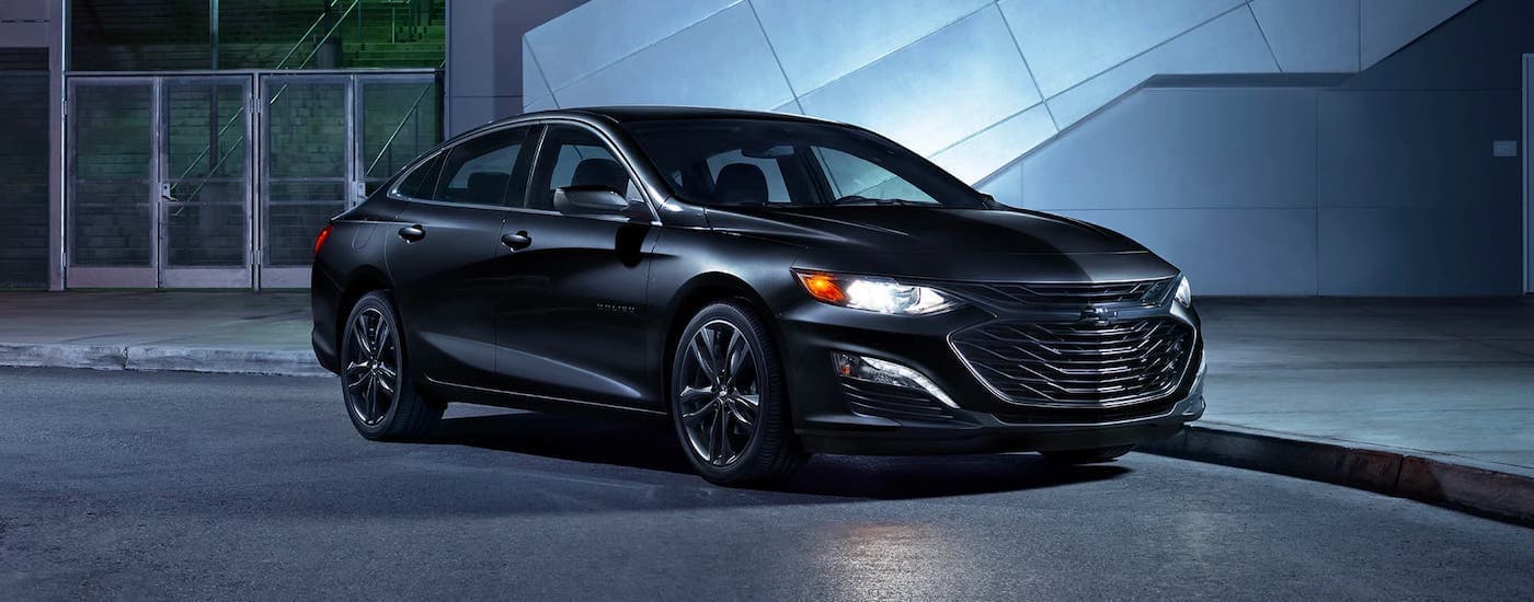 A black 2020 Chevy Malibu is shown from the side parked in front of a modern building.