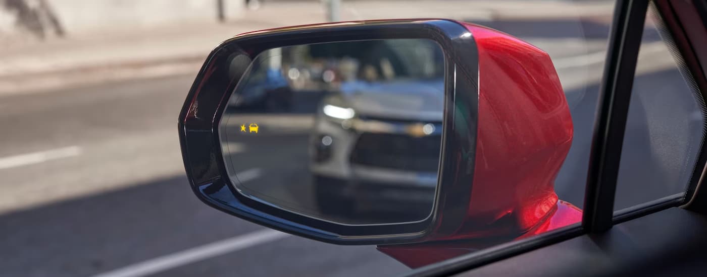 A silver 2023 Chevy Blazer is shown in the side mirror of a red SUV.
