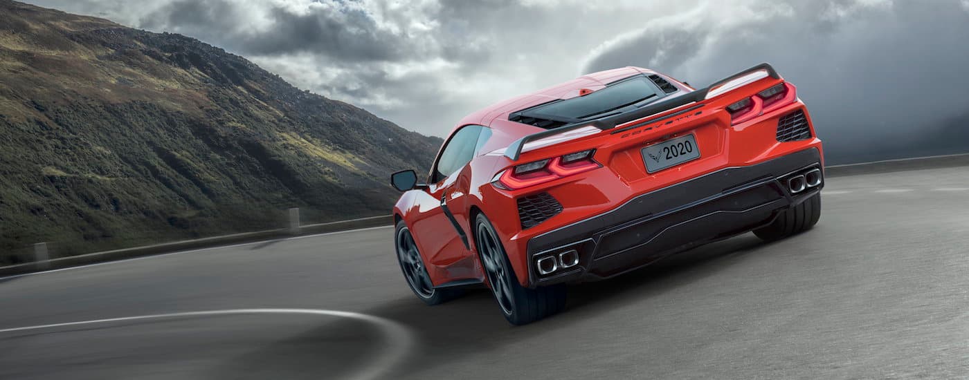 A red 2020 Chevy Corvette Stingray is shown from the rear rounding a corner on a mountain road.
