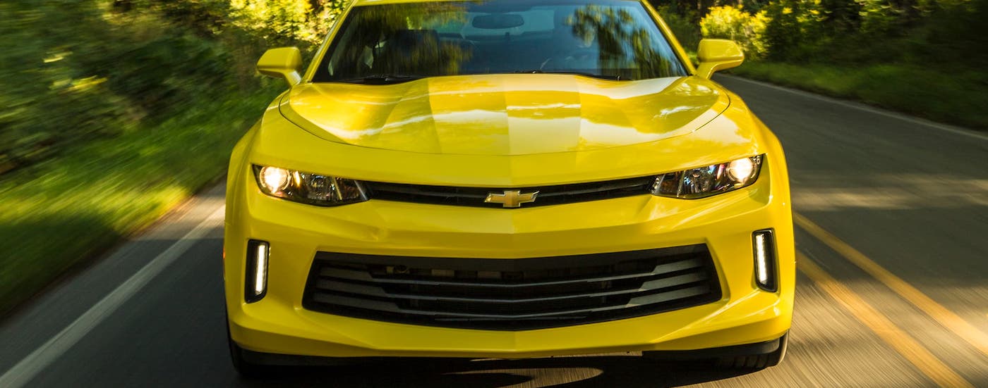 A yellow 2017 Chevy Camaro is shown from the front while driving on a tree-lined road.