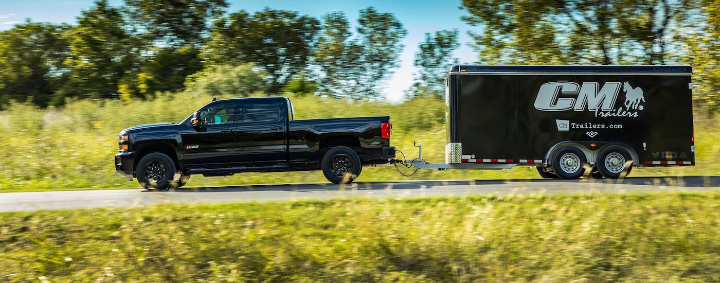 A black 2017 used Chevy Silverado 2500 is shown from the side towing a black enclosed trailer.
