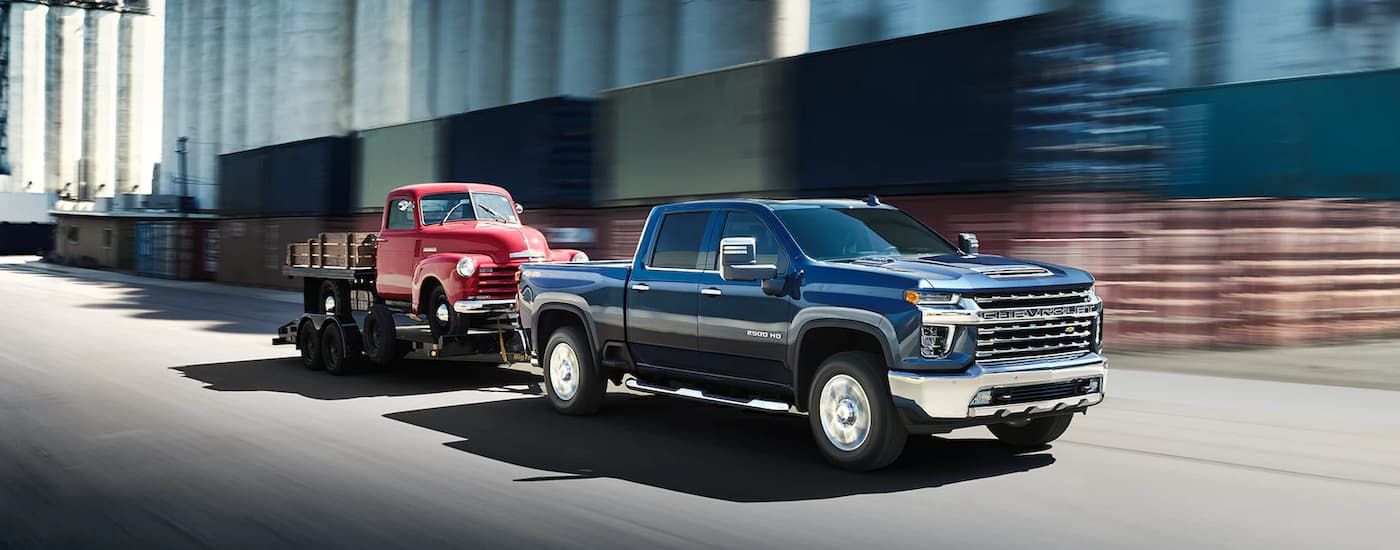 A blue 2022 Chevy Silverado 2500HD is shown towing a red truck down a city street.