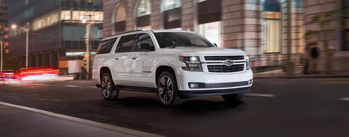 A white 2020 Chevy Suburban is shown driving on a city street.