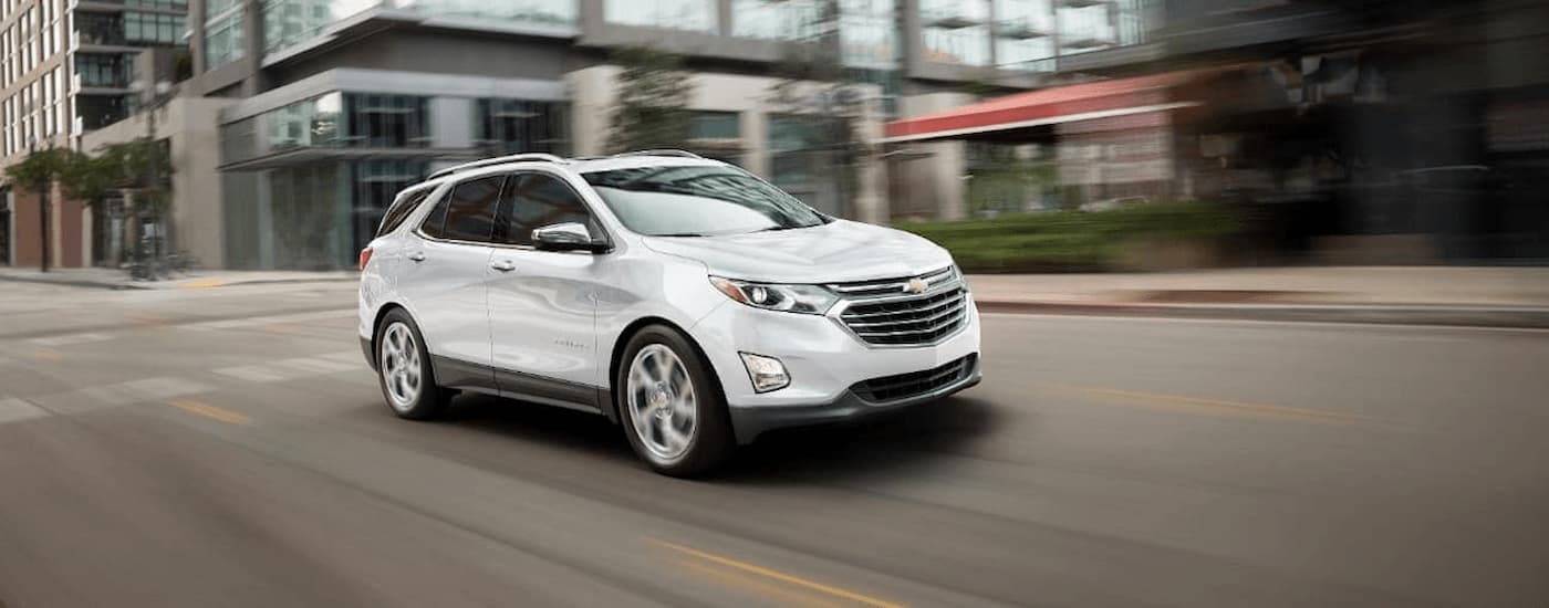 A white 2018 used Chevy Equinox for sale near Houston is shown driving on a city street.