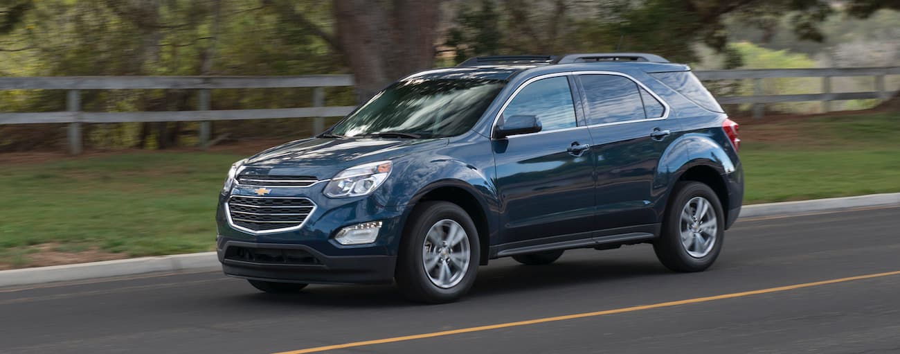 A blue 2017 used Chevy Equinox is shown from a side angle driving on a city street.