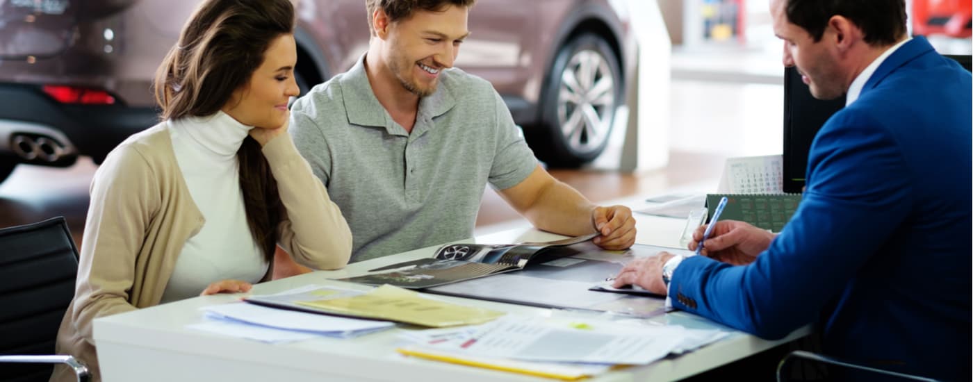 A car salesman is shown speaking to a couple about financing paperwork.