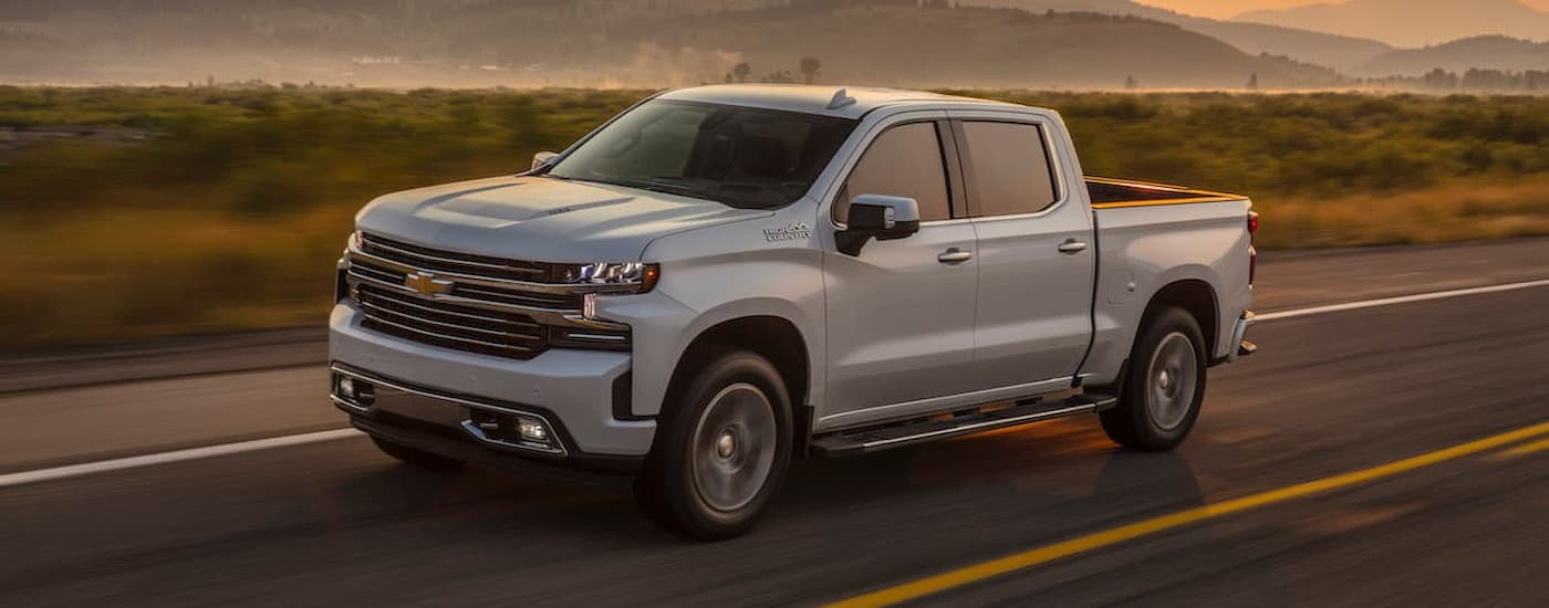 A white used 2019 Chevy Silverado 1500 High Country for sale near Aldine, TX is shown driving on an open road.